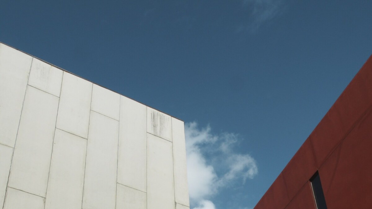 Low-angle view of white panelized building exterior panels adjacent to a red wall against a blue sky.